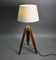 A modern wooden and brass telescopic tripod converted to a table lamp, with an off-white conical