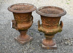 A pair of old weathered cast iron campagna urns, with twin handles raised on square pedestal