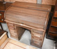 A compact light oak roll top desk, with nine drawers, raised on twin plinth bases to castors - by