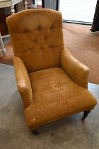 A Victorian armchair with worn velvet cover, on turned mahogany supports with brass and ceramic