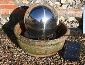 A contemporary stainless steel solar panelled spherical water feature in weathered terracotta bowl