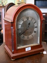 A mahogany-cased mantel clock with arched and silvered dial, brass loop top handle and bun feet,