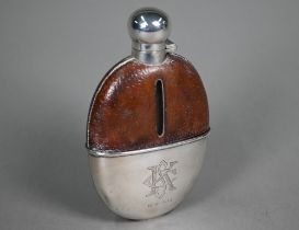 An antique glass spirit flask with leather shoulders, bayonet bun cover and detachable beaker,