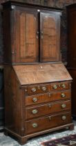 An 18th century oak bureau cabinet, the upper part with pair of panelled doors enclosing shelves,