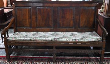 A Georgian oak four panel back settle, the shaped and swept arms over a rope seat (with later