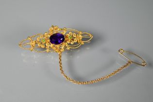 A Victorian 15ct gold brooch of open scroll form, set central oval purple stone with two peridot