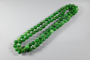 WITHDRAWN A row of uniform round jade beads, varying hues of green, double knotted throughout, 60 cm