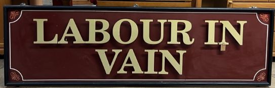 A large sign with a black frame and maroon ground, with raised letters "LABOUR IN VAIN",