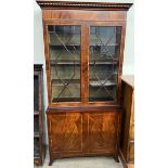 A reproduction mahogany bookcase with a moulded dentil cornice and two glazed doors,