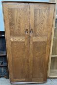 An Ercol light elm two door wardrobe, with panelled doors enclosing hanging space,