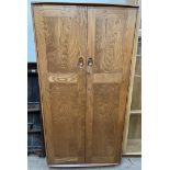 An Ercol light elm two door wardrobe, with panelled doors enclosing hanging space,