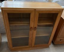 An Ercol light elm bookcase with a pair of bevelled glass doors on a plinth base, 91.