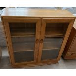 An Ercol light elm bookcase with a pair of bevelled glass doors on a plinth base, 91.