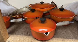 A collection of enamelled orange Le Crueset sauce pans,