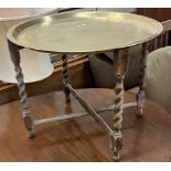 A brass topped coffee table of circular form with an oak barley twist folding base