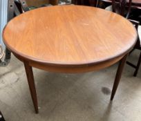 A mid 20th century teak extending dining table of circular form on tapering legs