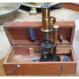 A brass monocular microscope with a black case and mahogany cabinet