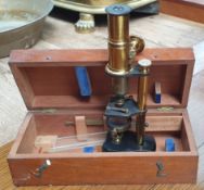 A brass monocular microscope with a black case and mahogany cabinet