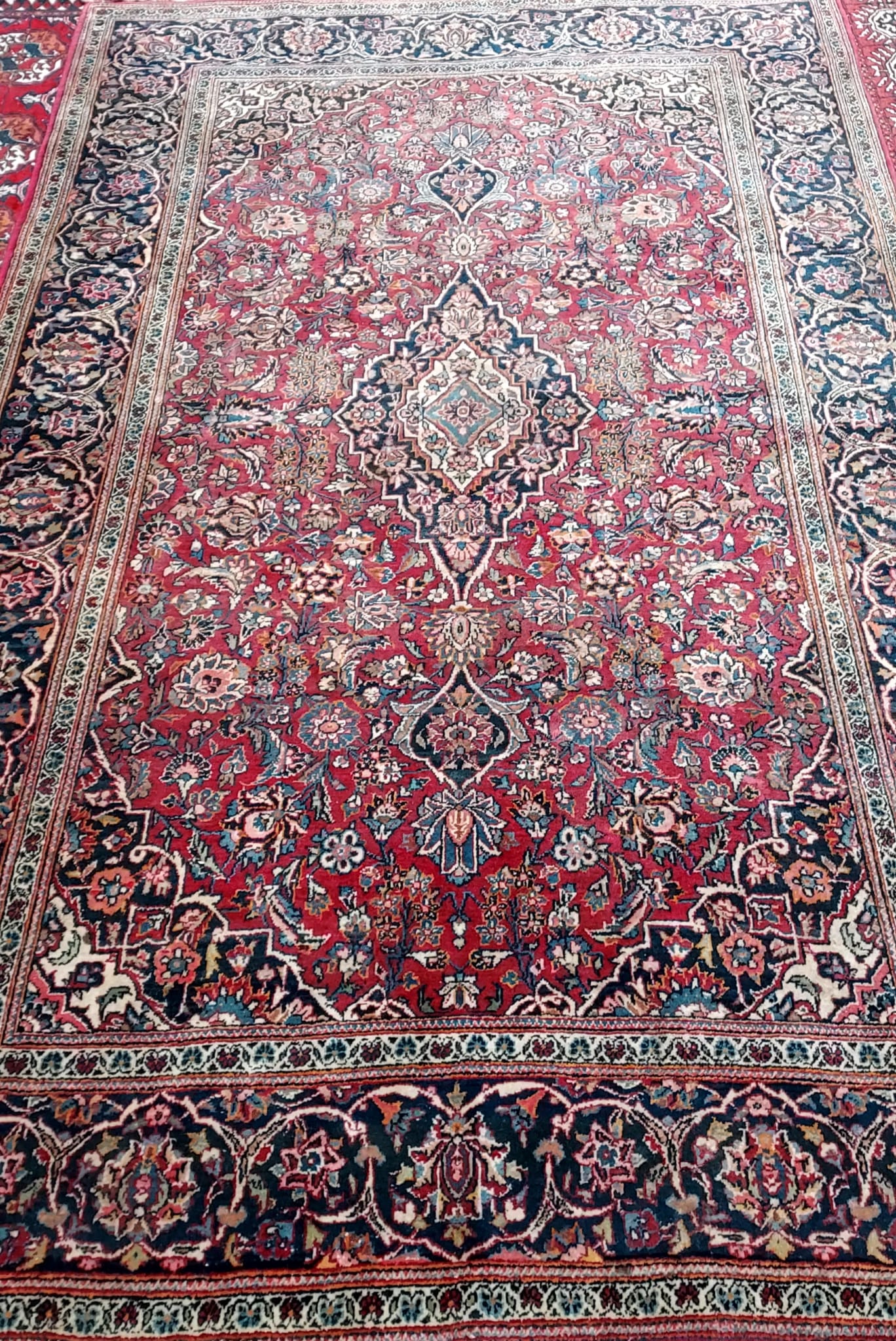 A red ground rug with a central medallion and scrolling flowers to a wide blue ground guard strip