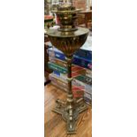 A gilt metal oil lamp with a tapering column on three legs with hoof feet and a shaped base,