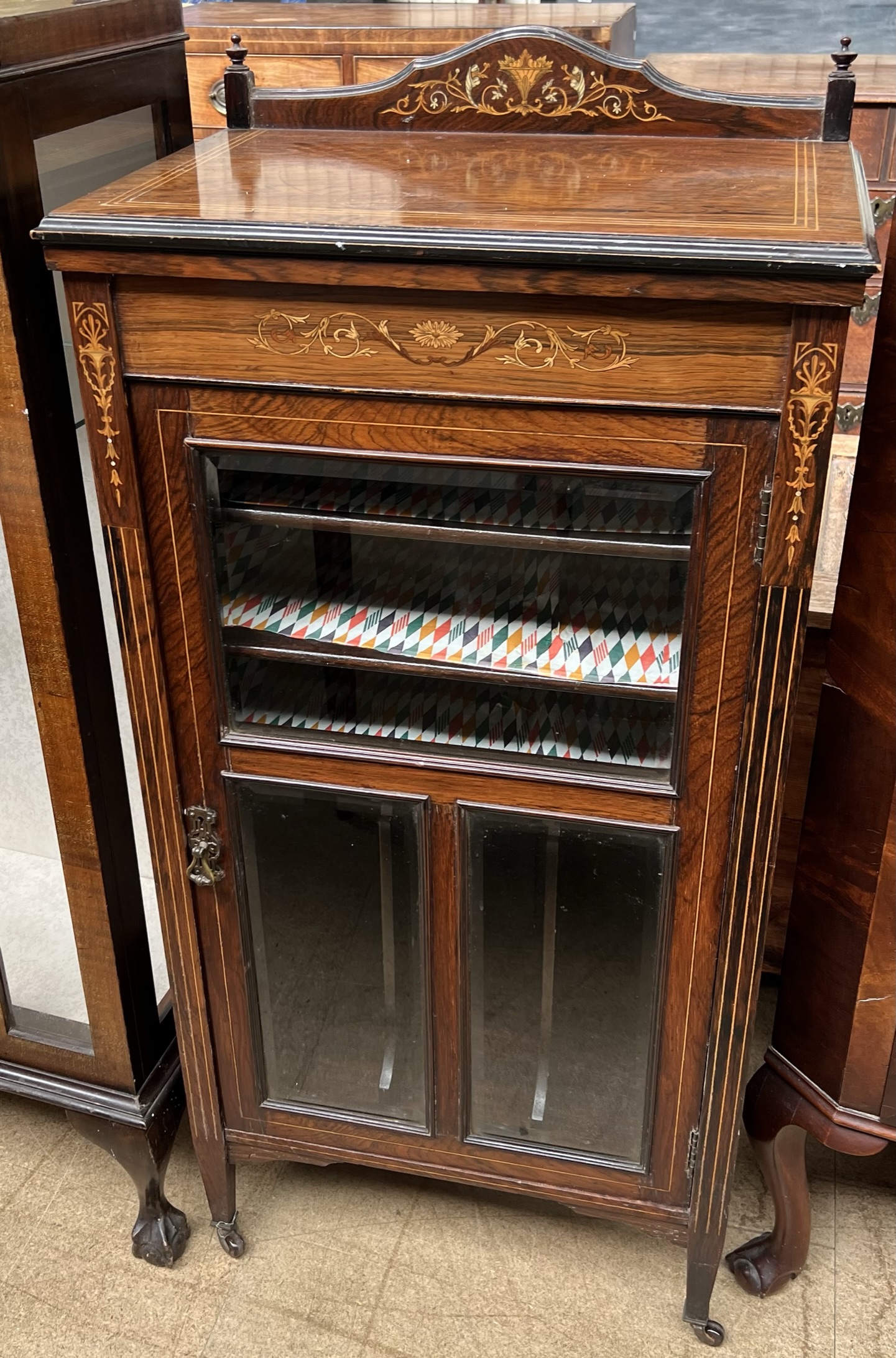 A late Victorian rosewood music cabinet with a shaped back above a glazed door with shelves and