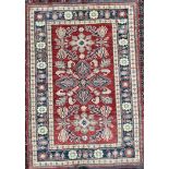 A Pakistan wool rug with a red ground, geometric patterns and cream and blue guard stripes,