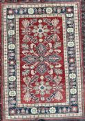 A Pakistan wool rug with a red ground, geometric patterns and cream and blue guard stripes,