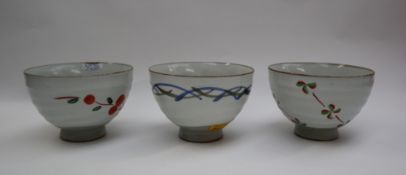 Three assorted stoneware footed bowls in the Chawan style, decorated with flowers and lines,