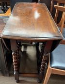 An early 20th century oak gateleg dining table with an oval top with drop flaps on barley twist