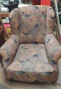 A large Victorian upholstered wing back armchair on turned feet and casters