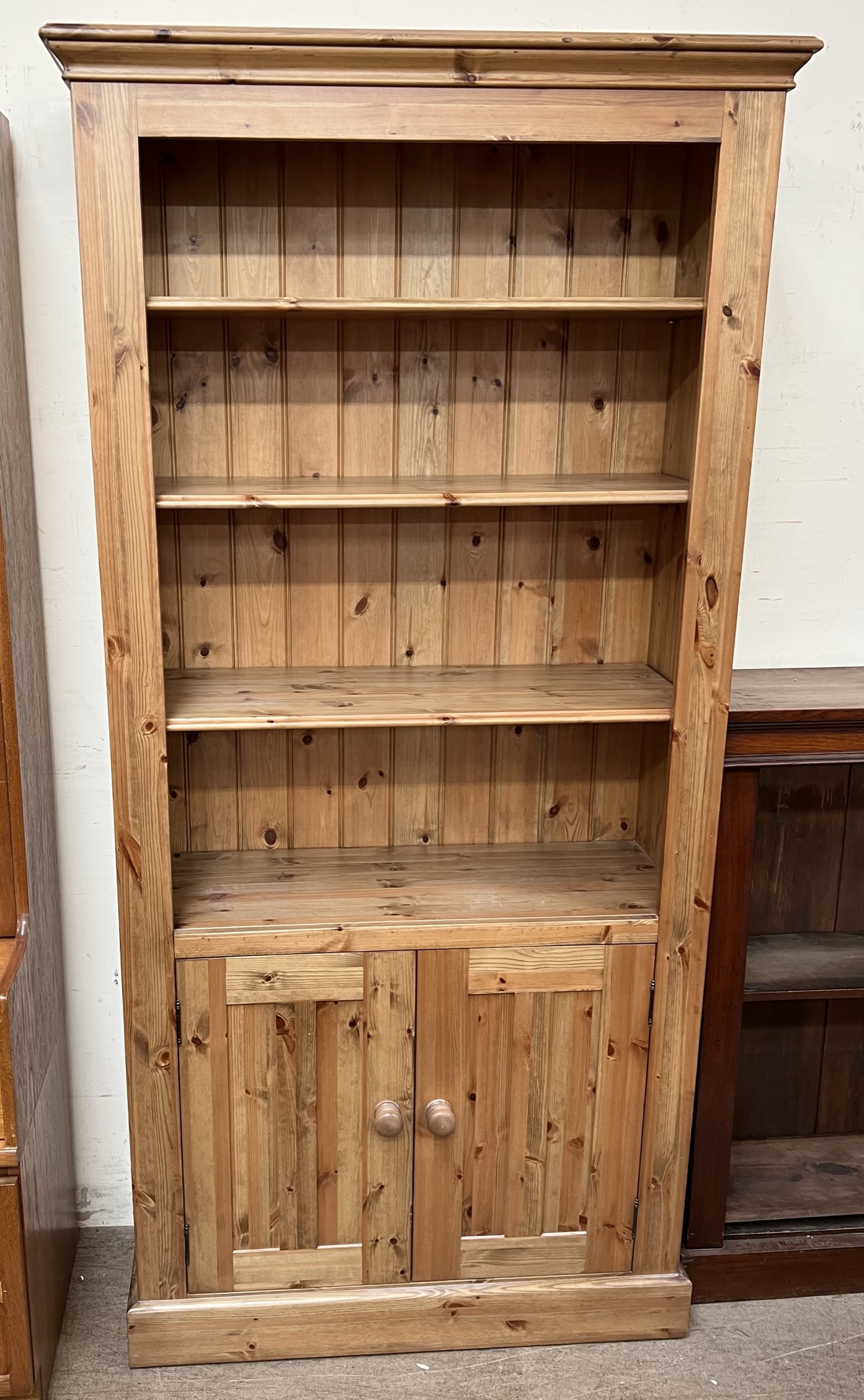 A pine bookcase with a moulded cornice above three shelves and two cupboards on a plinth