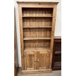 A pine bookcase with a moulded cornice above three shelves and two cupboards on a plinth