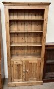 A pine bookcase with a moulded cornice above three shelves and two cupboards on a plinth