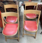 A set of four folding chairs with red vinyl seats