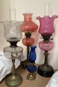 A cranberry glass oil lamp together with three other oil lamps