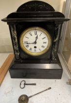 A black slate mantle clock with a bowed top and variegated columns on a plinth
