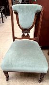 An Edwardian nursing chair with a pad upholstered back and seat on turned legs and casters