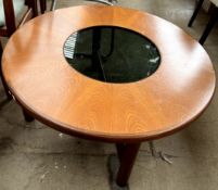 A teak coffee table of circular form with a smoked glass insert on cylindrical legs united by an X