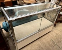 A shop display cabinet with chrome edges and white painted base cupboard