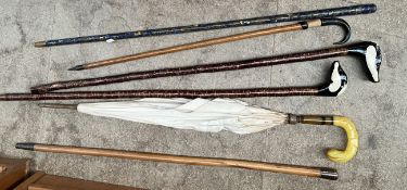 A white metal topped walking stick together with other walking sticks and a parasol
