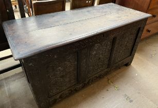 An 18th century oak coffer with a planked rectangular top and a three panel carved front on stiles