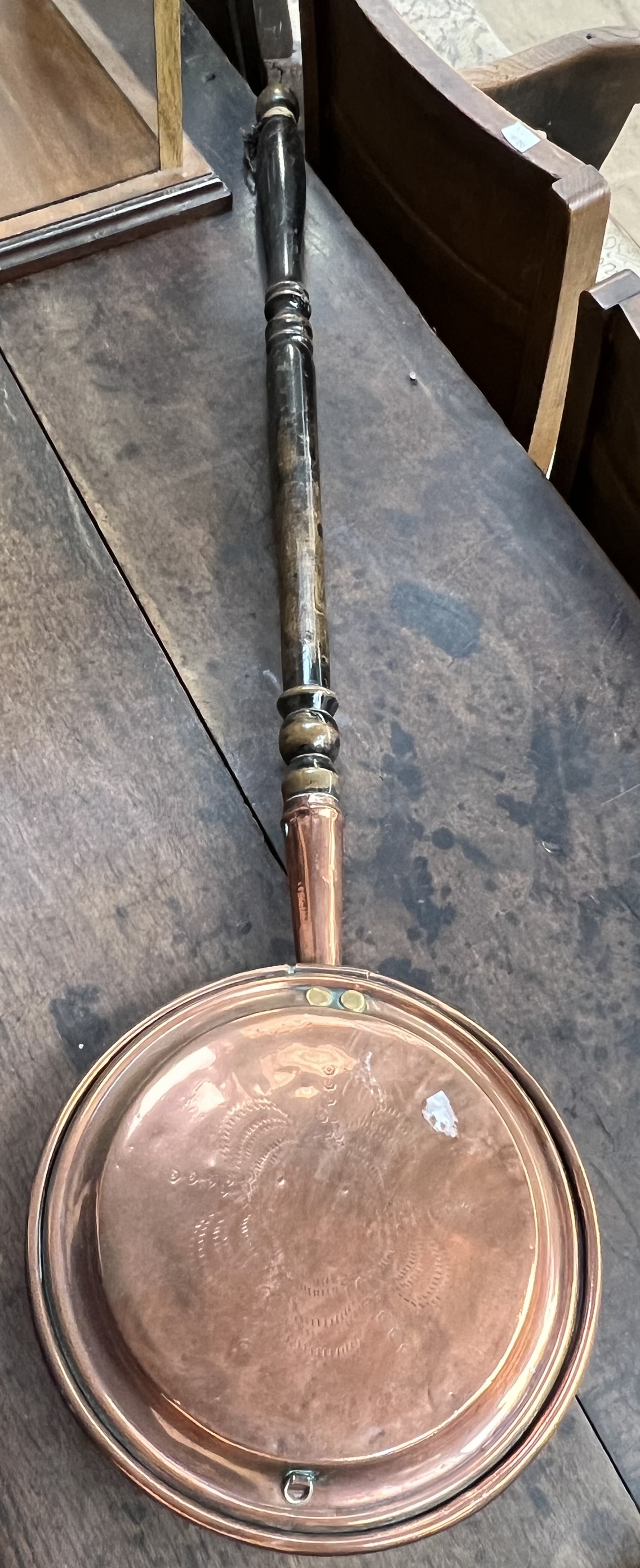 A copper bedwarming pan on a turned handle
