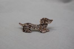 A bar brooch in the form of a dachshund, set with irregular cut diamonds, to a white metal setting,