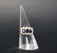 A sapphire and diamond cluster ring set with three oval dark blue sapphires surrounded by sixteen