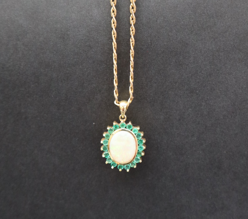 An emerald and opal pendant of oval form set with a central opal and nineteen emeralds to yellow