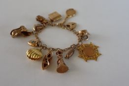 A 9ct gold charm bracelet set with numerous charms, including as kettle, medallion, lighthouse,