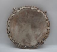 A George V silver waiter of circular form, with a shaped edge on four legs with pointed pad feet,