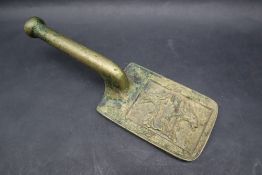 A bronze flat iron tool with a rectangular body decorated with figural heads on an integral handle,