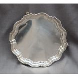 A George V silver salver of circular form with a shaped edge on three scrolling feet, Chester, 1932,