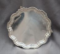 A George V silver salver of circular form with a shaped edge on three scrolling feet, Chester, 1932,